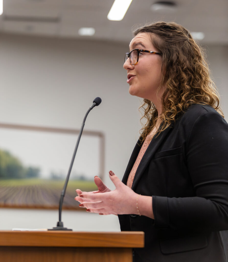 A female student with glasses stands in front of a microphone and speaks during a competition