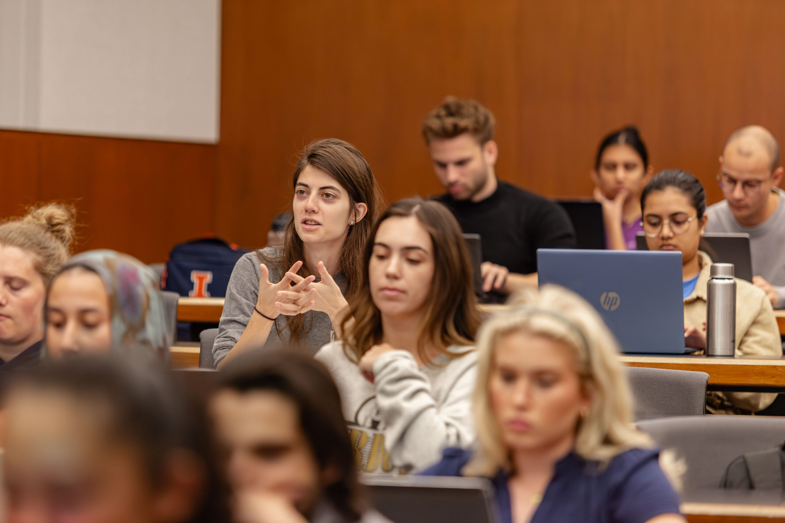 Female student asks a question in class. She is surrounded by other students.