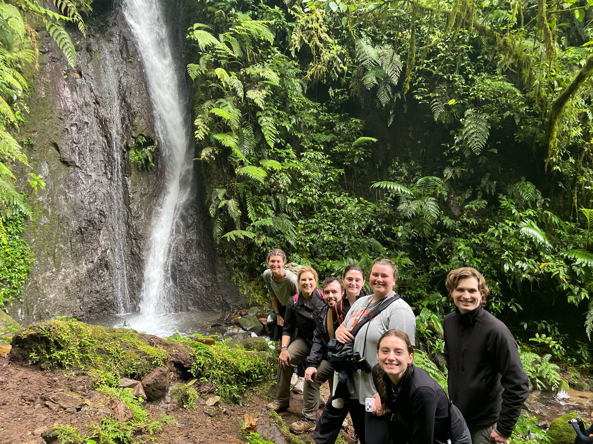 A group of students and Professor Heidi Hurd stop for a photo near a waterfall during a hike in Costa Rica, as part of the winter study abroad trip in 2026.