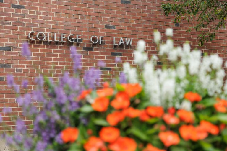 College of Law letters on brick building, with blue, orange, and white flowers in foreground