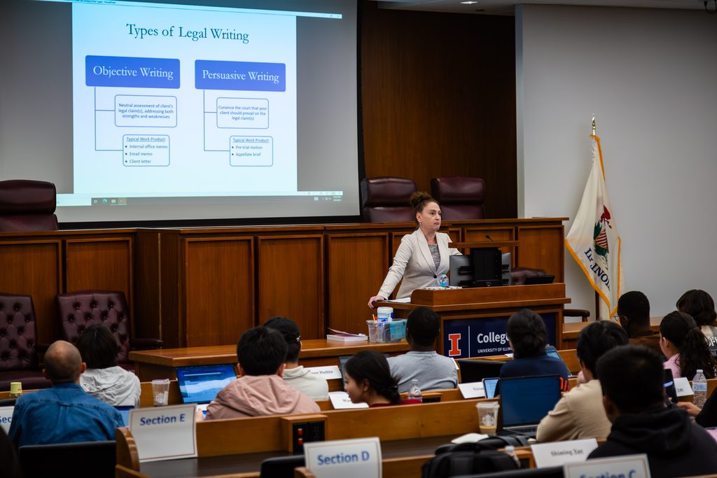 Professor Shannon Moritz stands at a podium in front of a screen, looking out at a classroom full of students.